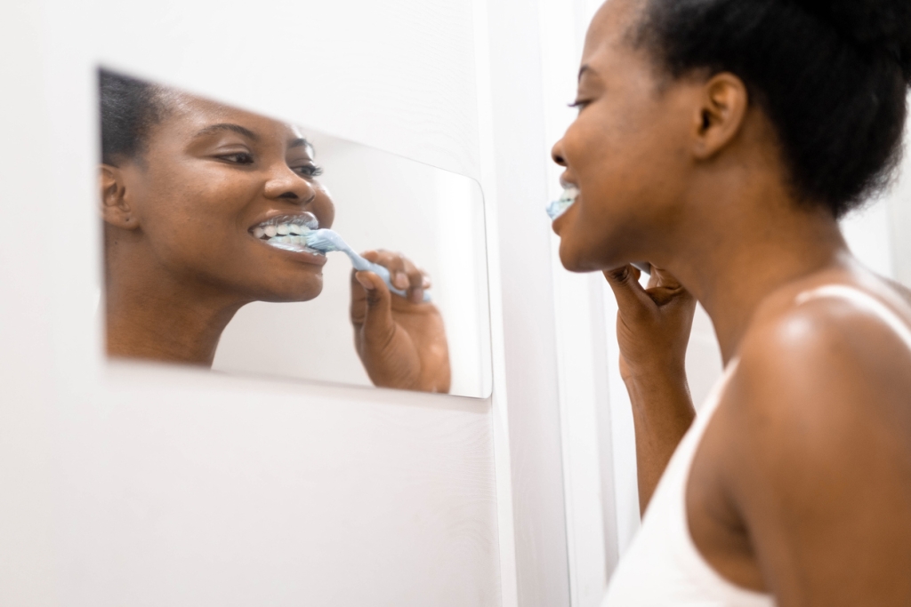 Portrait happy black African American girl brushing teeth in the bathroom. Morning routine with toothbrushes woman looking in mirror