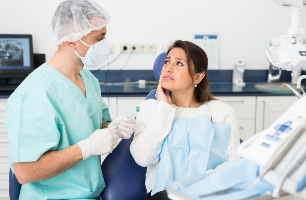 Unhappy hispanic patient woman having a toothache in dental chair at modern dental clinic